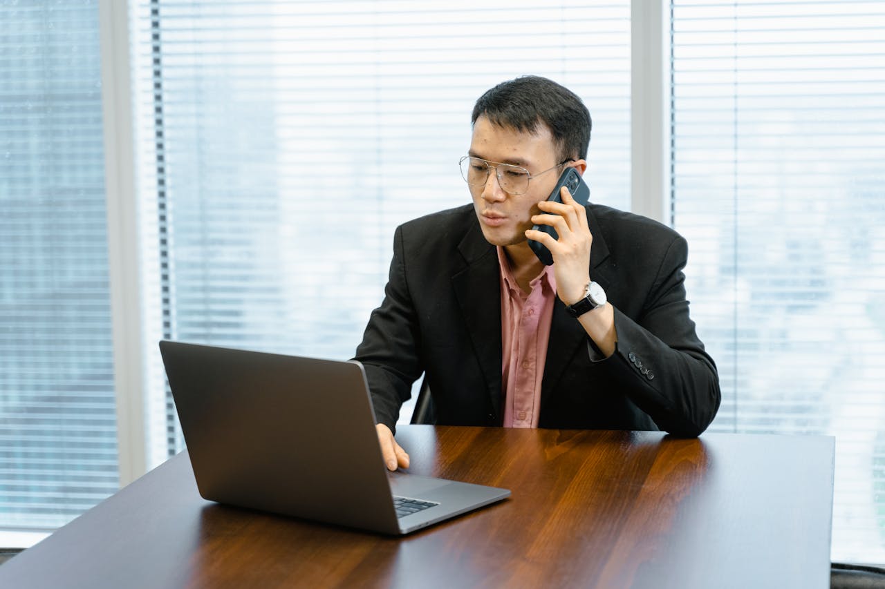 gallery-3 Businessman working remotely, talking on phone with laptop in office.