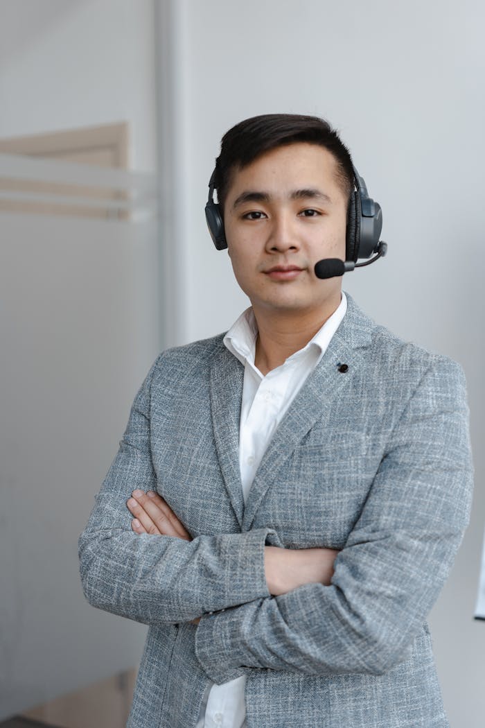 Asian male call center operator wearing a gray suit with a headset, providing customer service support.