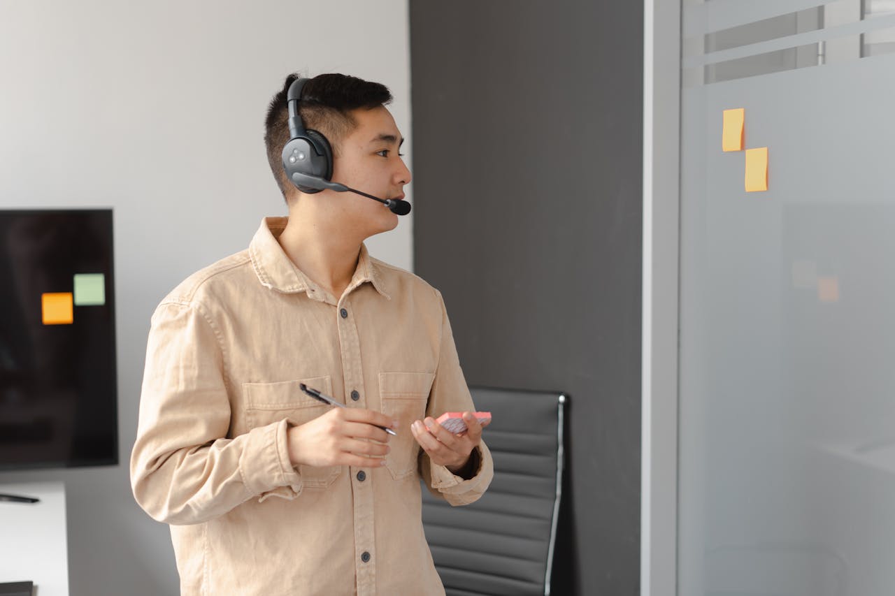 Professional Asian man working in call center holding pen and smartphone.