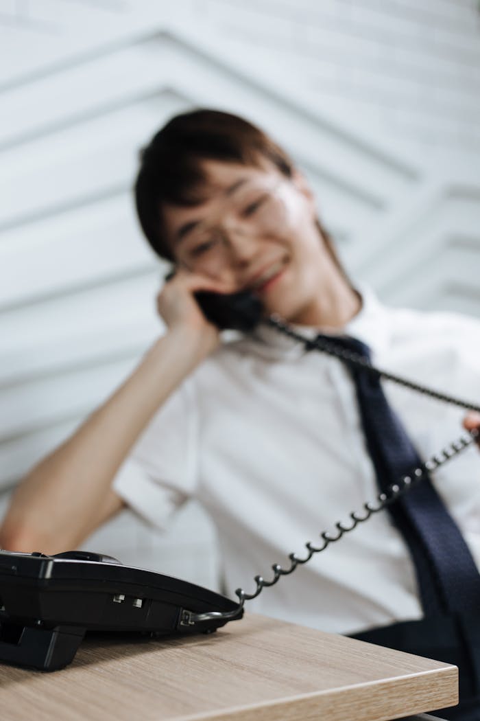 gallery-4 Young woman in an office setting, engaging in a phone call with a pleasant demeanor.